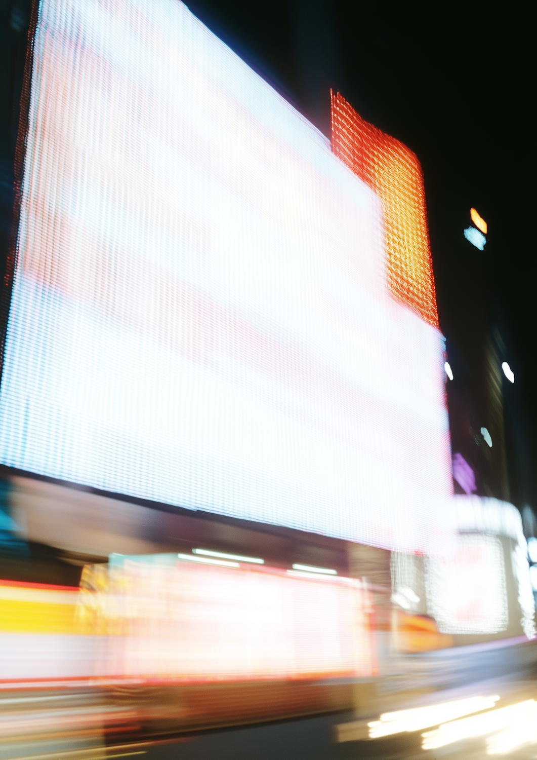 A blurred city street at night with bright billboards and streaking headlights